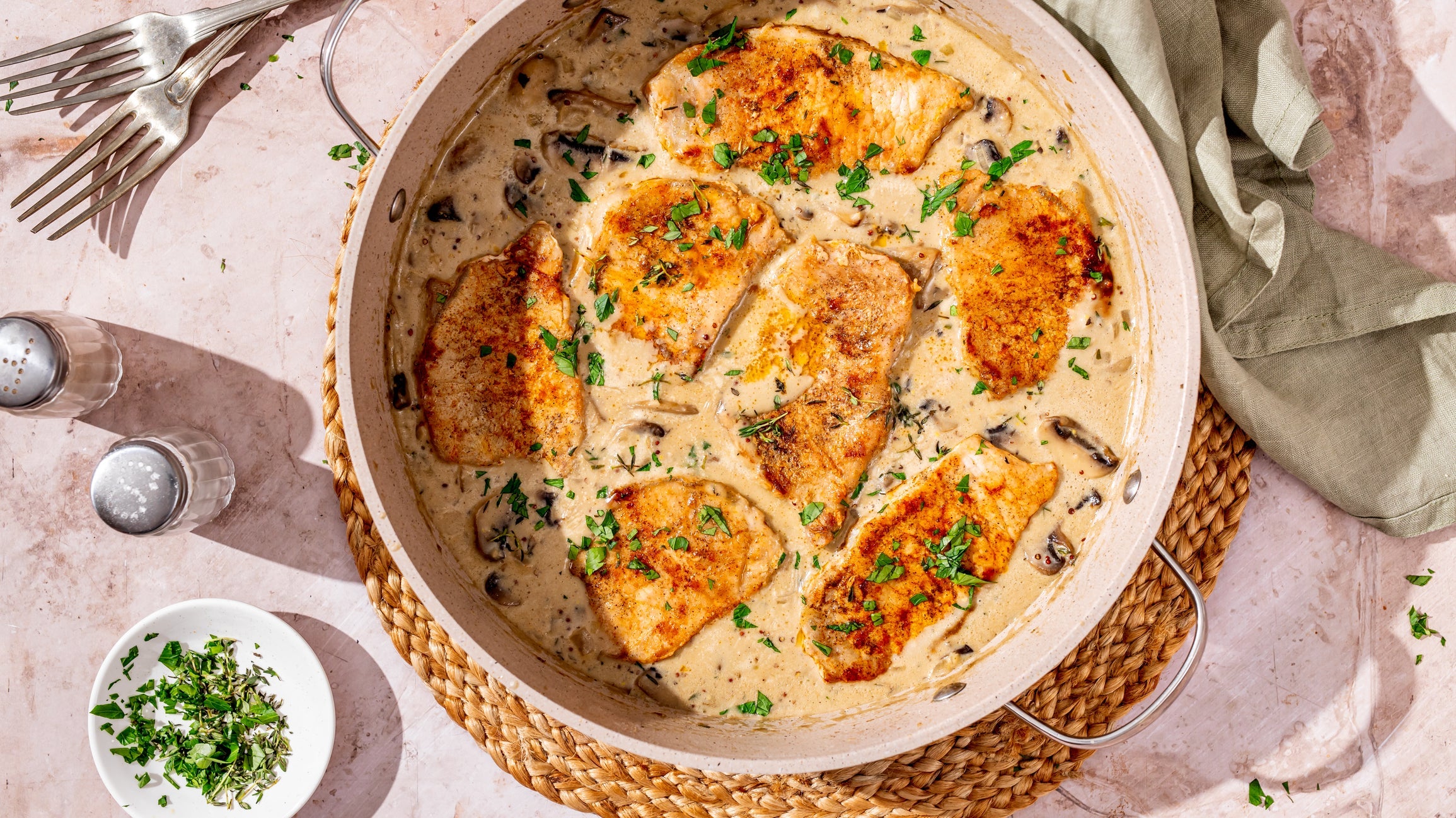 Herb-crusted Natural Heritage pork chop topped with creamy mushroom sauce on a rustic dinner plate